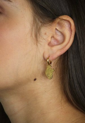 Pendientes de aro de oro con un colgante en forma de corazón con detalles intrincados, colgando del lóbulo de la oreja sobre un tono de piel neutro.