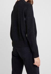 Stickad svart tröja med rund halsringning, ribbade ärmslut och fåll, samt mjuk textur. Bärs med mörka jeans och har en avslappnad passform.