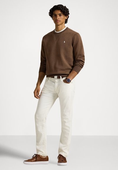 Brązowa bluza, białe dżinsy i brązowe trampki. Bluza ma logo na piersi, dopasowany krój oraz okrągły dekolt z fakturowaną powierzchnią.