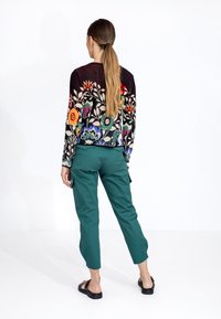 Pull floral multicolore avec un fond noir porté sur un pantalon cargo vert. La tenue présente une coupe décontractée et des sandales plates.