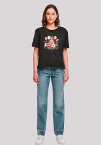 Black cotton t-shirt featuring a floral design with pink and white tulips. Paired with light blue denim jeans and white sneakers.