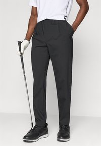 Melnas golfa bikses ar gludu audumu, plecu priekšpusi un josta cilpām. Apvienotas ar baltu krekla un melnām golfa kurpēm, tur rokā golfa nūju.