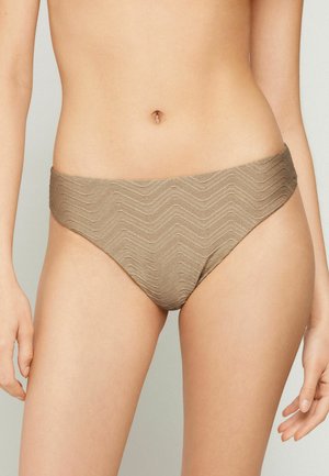 Mujer con braguitas de bikini beige de corte alto y textura con un sutil patrón en chevron, mostrada desde la cintura hasta la parte superior de los muslos.