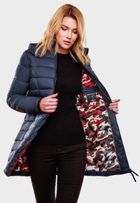 Veste en duvet marine avec capuche. L'intérieur présente un motif camouflage rouge, gris et noir. Texture lisse, fermeture éclair et poches latérales.