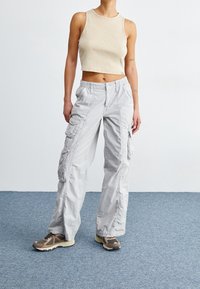 Ljust grå cargobyxor med flera fickor och en avslappnad passform, i kombination med en kortärmad beige linne och bruna sneakers med ljusa detaljer.