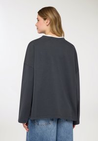 Maglia oversize a maniche lunghe di colore grigio scuro con scollo rotondo e spalle scese, caratterizzata da una texture liscia e un orlo dritto.