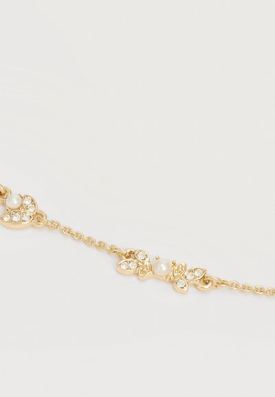 Λεπτό χρυσό βραχιόλι με ρυθμίσεις σε σχήμα φύλλου που κρατούν μικρούς διαυγείς κρυστάλλους και μια μοναδική στρογγυλή λευκή πέρλα στο κέντρο.