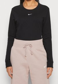 Svart långärmad t-shirt med vitt Nike-logga, kombinerad med ljusrosa joggingbyxor med dragsko och subtilt logotyp.