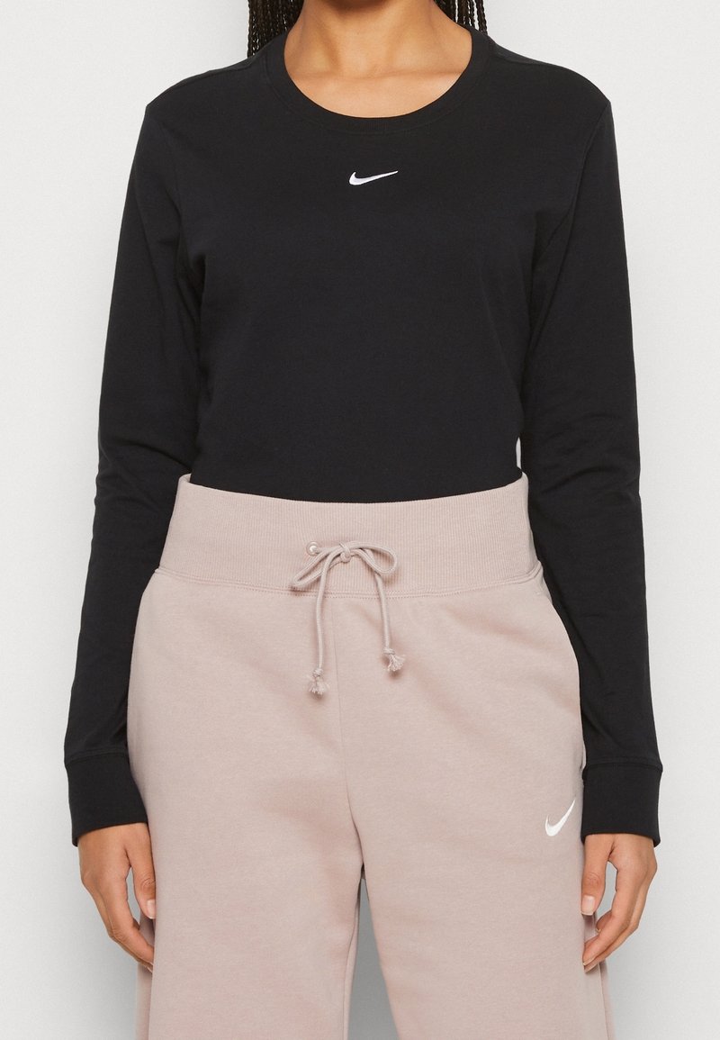 Svart långärmad t-shirt med vitt Nike-logga, kombinerad med ljusrosa joggingbyxor med dragsko och subtilt logotyp.