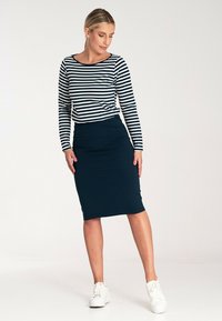 Pasiasty, długi rękaw w kolorze granatowym i białym, zestawiony z dopasowaną granatową spódnicą ołówkową; modelka nosi białe trampki. Gładki materiał, dopasowany krój.