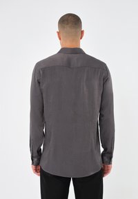 Long-sleeve, button-up shirt in dark gray with textured fabric. Features a classic collar and cuffs with buttons. Tailored fit, curved hem.