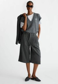 Gilet grigio lavorato a maglia su una maglietta bianca, abbinato a culotte grigie a righe e scarpe slingback nere con punta. Insieme elegante e moderno.