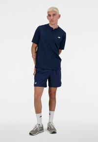 Navy athletic shirt with short sleeves and a henley collar, paired with matching shorts. Shoes are light gray with darker accents, white socks.