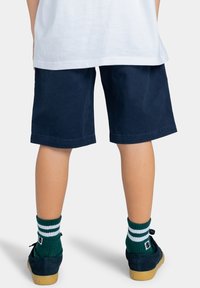 Navyblauwe katoenen shorts met een losse pasvorm, gecombineerd met groene geribde sokken met witte strepen en navyblauwe schoenen met gomzolen.