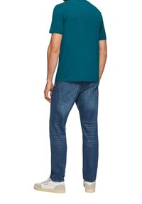 Teal lyhythihainen polo-paita yhdistettynä tummansinihin farkkuihin ja valkoisiin lenkkareihin. Farkuissa on klassinen malli ja hieman väriä loiventava vaikutus.