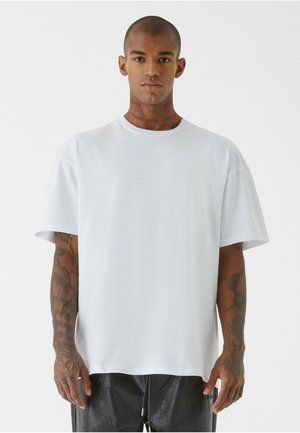 Hvid oversized t-shirt med korte ærmer, lavet af glat stof. Har en rund halsudskæring og hænger løst over kroppen.