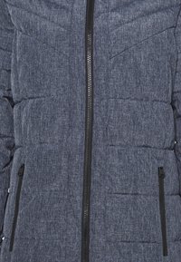 Chaqueta acolchada de marinero con cremallera en la parte frontal, dos bolsillos laterales y una tela texturizada con un patrón sutil. Cremallera negra y acentos.
