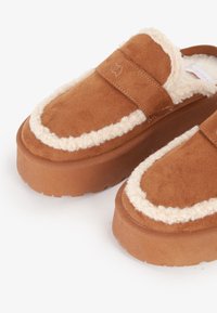 Scarpe slip-on in suede marrone con una morbida fodera crema, suole a piattaforma rialzate e dettagli cuciti lungo i bordi.