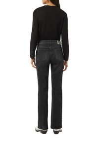 Schwarzes Langarmoberteil kombiniert mit dunkelgrauen Schlagjeans. Die Jeans haben Gesäßtaschen und ein Etikett am Bund. Glatte Textur.