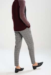 Multikleurige kabelgebreide trui in bordeauxrood, grijs en roze, gecombineerd met grijze geruite broek en zwarte platte schoenen. Gestructureerde stof en op maat gemaakte pasvorm.