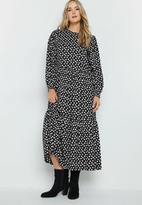 Vestido negro con lunares, de mangas largas, escote redondo, falda en capas y aberturas laterales, combinado con botas negras hasta la rodilla.