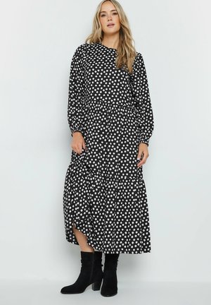 Black polka dot dress with long sleeves, round neckline, tiered skirt, and side slits, paired with knee-high black boots.