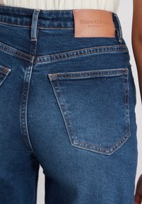Dunkelblaue Denim-Jeans mit orangefarbenen Nähten und einem Lederetikett an der Taille. Mit zwei klassischen Gesäßtaschen ausgestattet.