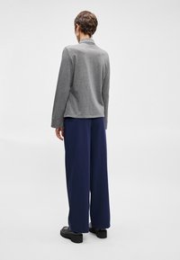 Γκρι μπλούζα με μακριά μανίκια και γιακά, σε συνδυασμό με φαρδιά μπλε παντελόνια. Με λεία υφή, χαλαρή εφαρμογή, διαθέτει γυρισμένα μανίκια και απλό σχέδιο.