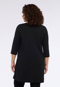 Czarna sukienka o długości do kolan z elastycznej tkaniny, z rękawami do połowy przedramienia, prostym okrągłym dekoltem i gładkim szwem na plecach.