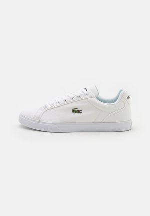 Baltas auduma kedas ar gumijas zoli, ar zaļu Lacoste krokodila logo un tīru šņorēšanu. Minimālistisks dizains ar noapaļotu purngalu.