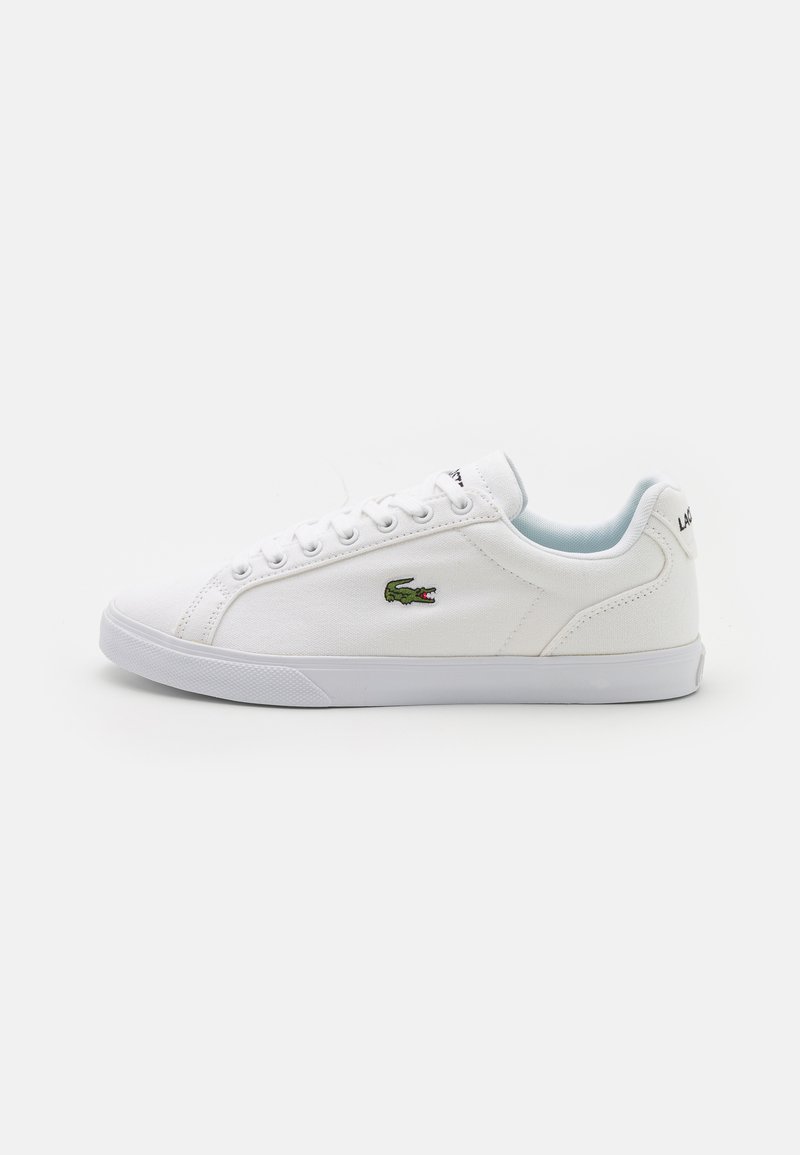 Hvite kanvas joggesko med gummisåle, med en grønn Lacoste krokodillelogo og rene snøringer. Minimalistisk design med rund tå.