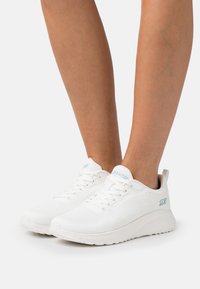 Weiße Sportschuhe aus atmungsaktivem Mesh, mit strukturiertem Obermaterial, hellblauen Akzenten und einer gepolsterten Sohle für Komfort.