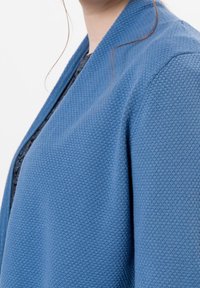 Cárdigan texturizado azul con un tejido suave y entrelazado. Presenta un diseño moderno de frente abierto y detalles de cuello de canalé.