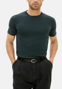 Dark green fitted short-sleeve t-shirt in a smooth, lightweight fabric, paired with black trousers and a black belt with a silver buckle.