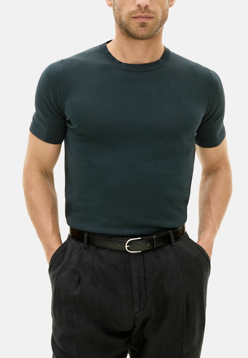 Dark green fitted short-sleeve t-shirt in a smooth, lightweight fabric, paired with black trousers and a black belt with a silver buckle.