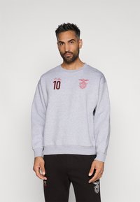 Sudadera gris de manga larga, con puños acanalados, cuello redondo, número "10" bordado en rojo y logotipo en el pecho. Corte casual, textura suave.