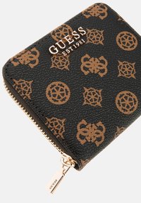 Sort tekstureret pung med lynlås, der har et brunt logo-mønster og metallisk guldaccentuer, herunder "GUESS"-logoet.