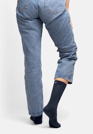 Marineblaue, knielange Socken mit elastischem Bündchen, getragen mit hellblauen Jeans. Die Socken haben ein kleines Logo an der Oberseite und eine glatte Textur.