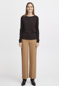 Pull noir à manches longues, coupe oversized, assorti à un pantalon beige taille haute à jambe droite et des bottines noires. Design simple, matériel minimal.