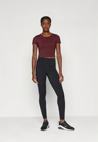 Vinröd kort t-shirt och svarta högmidjade leggings. Modellen bär svarta sportskor. Minimalistisk design, slät tygstruktur.