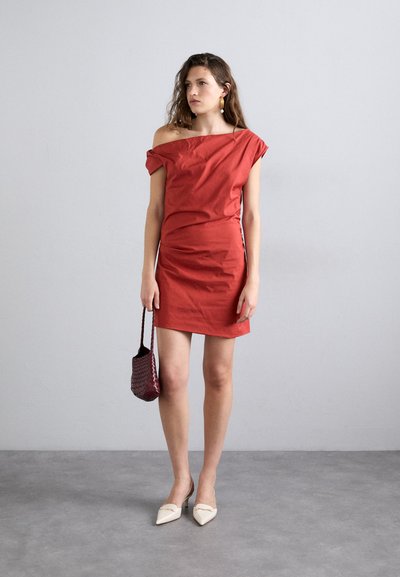 Rochie scurtă roșie, cu umerii la vedere, cu o siluetă ajustată, realizată dintr-un material neted. Asortată cu pantofi albi cu vârf ascuțit și o geantă mică burgund.