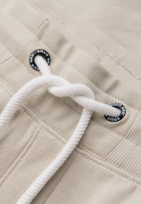Ceinture en tissu beige avec cordon blanc inséré dans des œillets métalliques noirs marqués « ombre wear ».