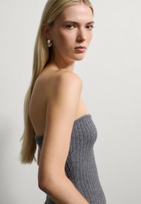 Top strapless de canalé gris con silueta ajustada. La modelo tiene el cabello largo y rubio y lleva grandes pendientes de plata. Fondo neutro.