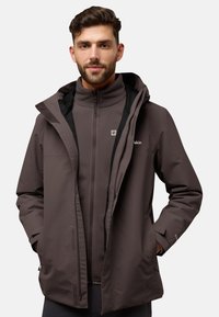 Bruine waterdichte jas met capuchon, gelaagd over een ritsfleece. Bevat zakken en een logo op de borst, gemaakt van zacht textiel.