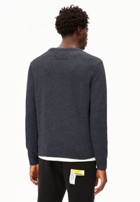 Pull sombre en navy avec un design de tricot texturé, des poignets et un ourlet côtelés, et un détail de étiquette minimaliste dans le dos. Coupe slim avec un col rond.