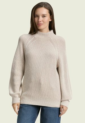 Beige gestreifter Pullover mit hohem Kragen, langen Ballonärmeln und einer lockeren Passform, kombiniert mit blauen Denim-Jeans.