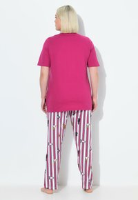 Różowy t-shirt z krótkim rękawem i zaokrąglonym dekoltem, zestawiony z białymi spodenkami do piżamy ozdobionymi pionowymi paskami i ilustracjami psów.