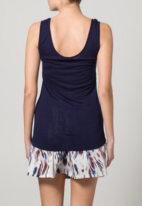 Top senza maniche blu navy con scollo a goccia, abbinato a una gonna fluida e patterned nei toni del bianco, blu navy e rosso. Tessuto morbido.