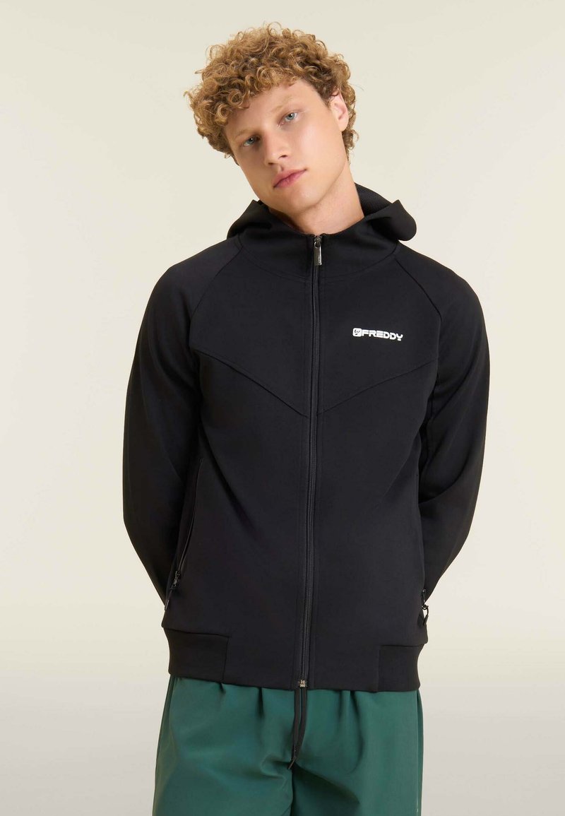 Sudadera deportiva negra con cremallera y cuello alto, bolsillos con cremallera y un logotipo blanco en el pecho. Cuenta con una tela suave y elástica.