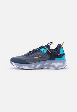 Marineblauwe en grijze Nike sneaker met blauwe en beige accenten, een patroon op het zijpaneel, treklabel en witte getextureerde zool.